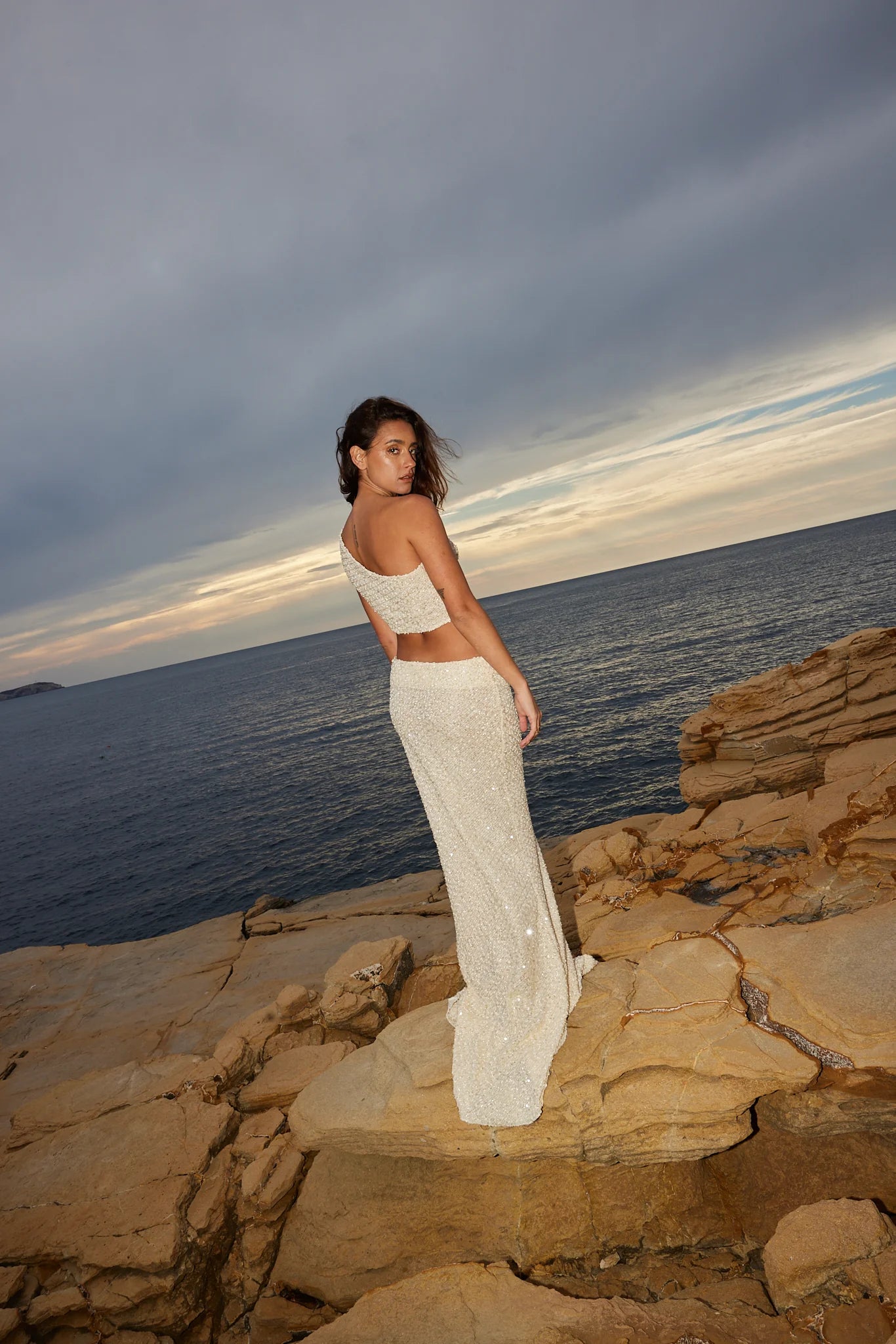 Ivory sequin crop top and maxi skirt set on model by rocky coastline at sunset — Label Loft London | Endless UAE