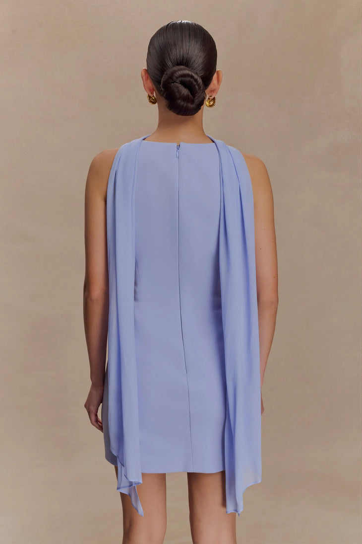 Rear view of model wearing light blue sleeveless mini dress with draped cape overlay and back zipper closure — Meshki | Endless UAE