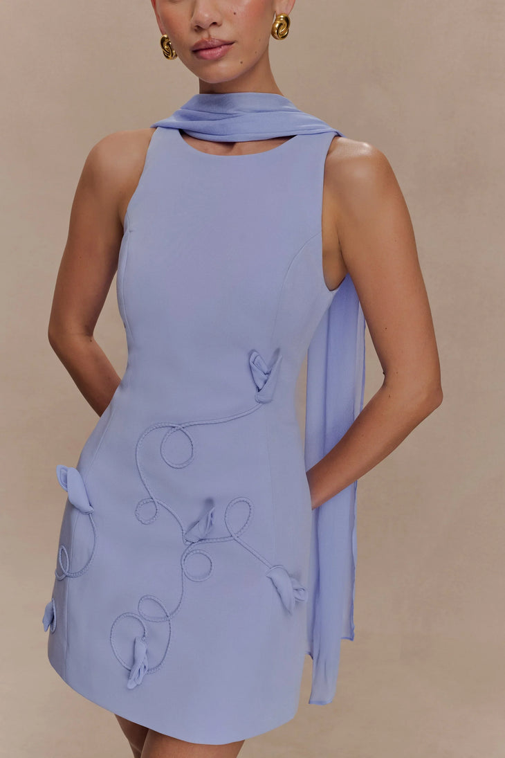 Model wearing a periwinkle blue sleeveless mini dress with circular embroidery, twisted collar detail and side ties — Meshki | Endless UAE