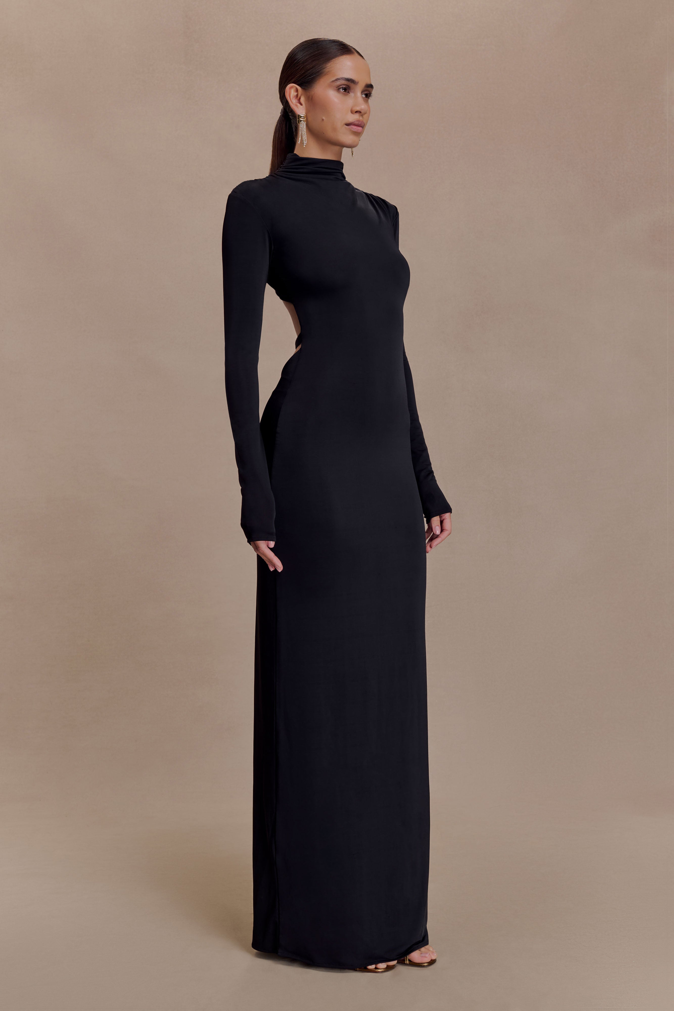 Black slinky maxi dress with high neck, long sleeves, and side cutout detail on model against neutral background — Meshki | Endless UAE