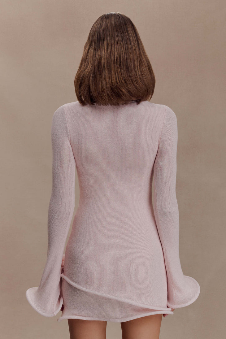 Rear view of woman wearing light pink ribbed knit mini dress with long sleeves and flared hem against beige background — Meshki | Endless UAE