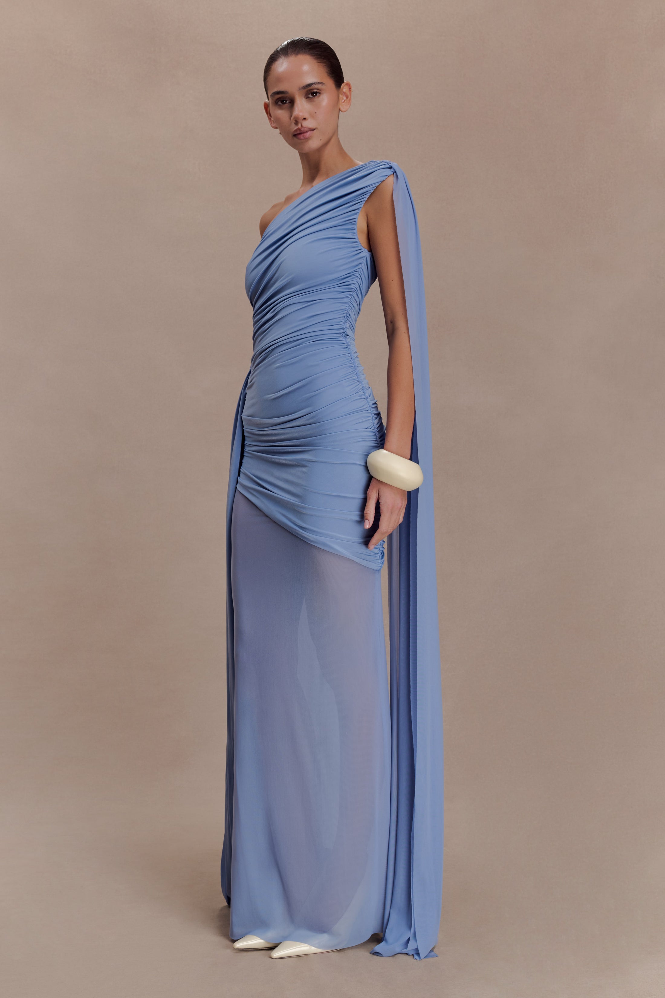 Woman wearing periwinkle blue one shoulder maxi dress with draped fabric detail and cream clutch — Meshki | Endless UAE