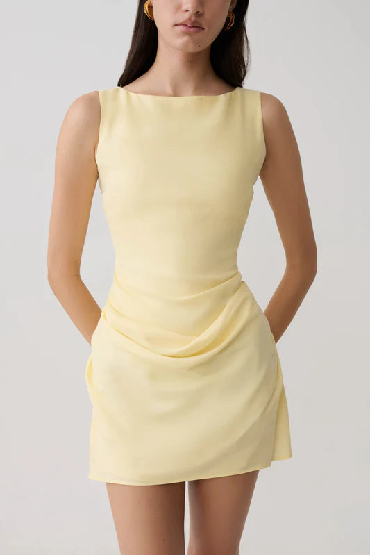 Woman modeling pale yellow sleeveless mini dress with draped side detail and white sandals — Meshki | Endless UAE