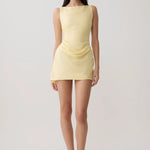 Woman modeling pale yellow sleeveless mini dress with draped side detail and white sandals — Meshki | Endless UAE