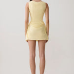Woman modeling pale yellow sleeveless mini dress with draped side detail and white sandals — Meshki | Endless UAE