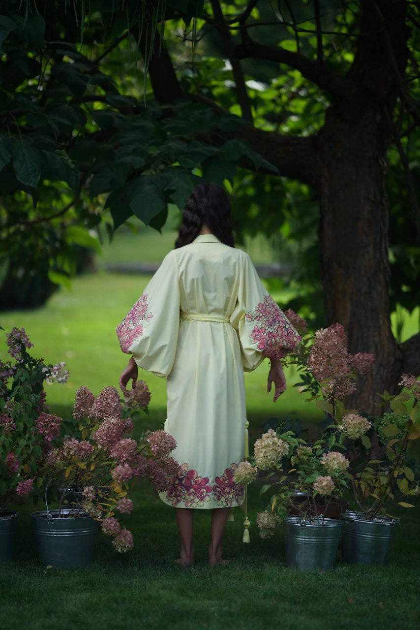 Woman wearing ivory cotton caftan with pink floral embroidery standing in garden with hydrangeas — Yuliya Magdych | Endless UAE