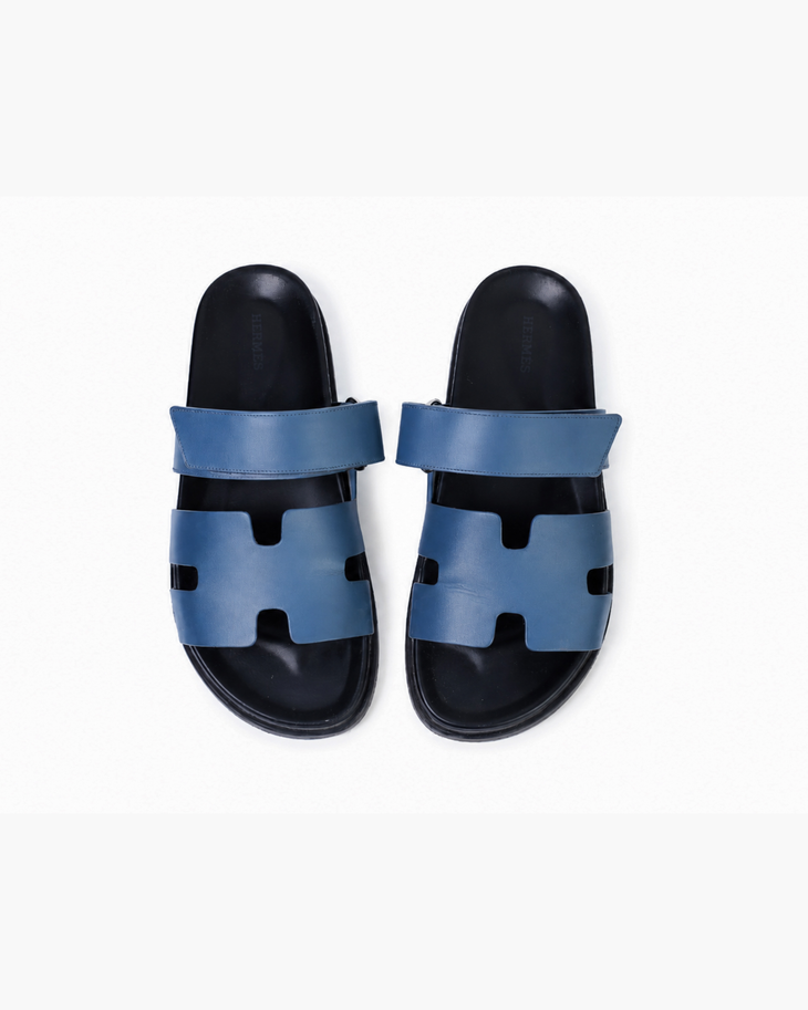 Black leather slide sandals with cutout straps displayed on orange box — Hermès | Endless UAE