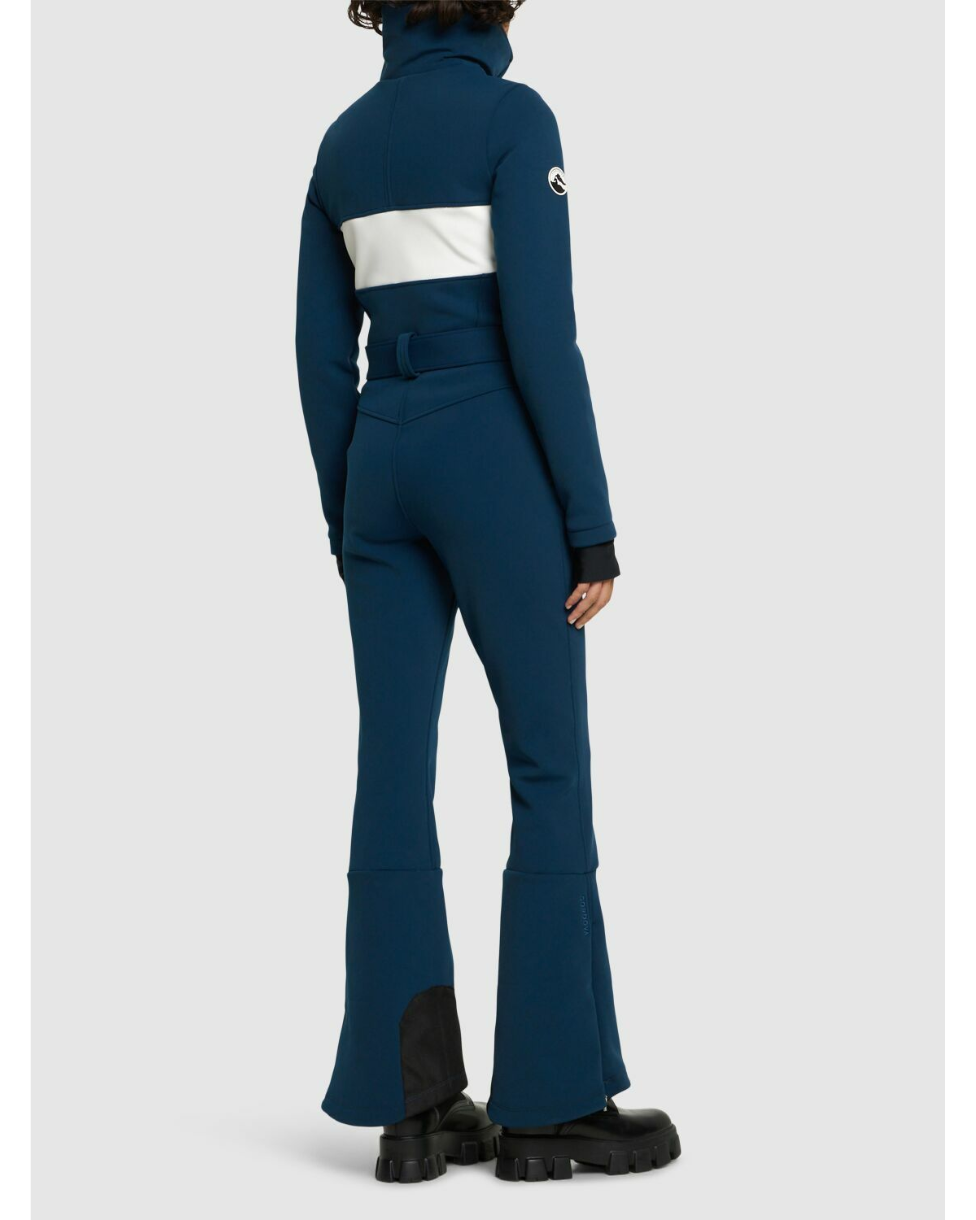 Woman wearing navy and white colorblocked ski jumpsuit with belt and black boots — Cordova | Endless UAE