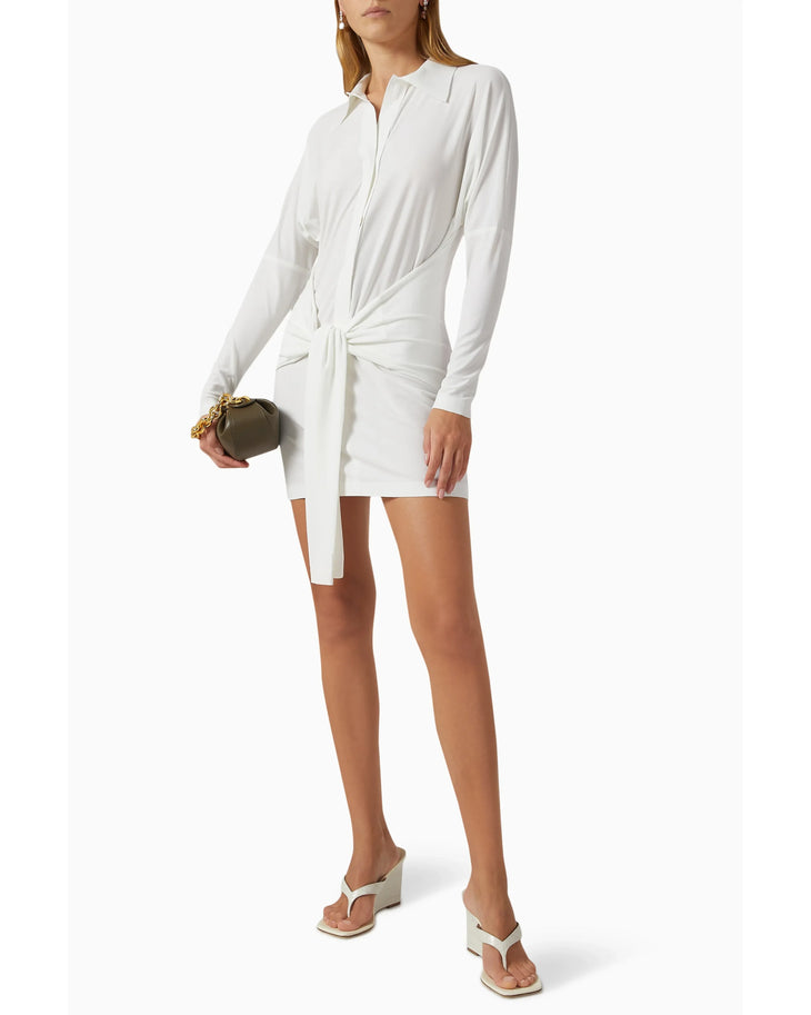 Woman wearing white long-sleeve shirt dress with front tie detail and white slide sandals — Norma Kamali | Endless UAE