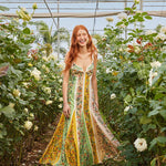 Woman wearing a colorful striped maxi dress with floral print standing in greenhouse surrounded by white flowers — Farm Rio | Endless UAE