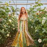 Woman wearing a colorful striped maxi dress with floral print standing in greenhouse surrounded by white flowers — Farm Rio | Endless UAE