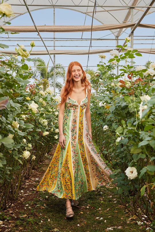 Woman wearing a colorful striped maxi dress with floral print standing in greenhouse surrounded by white flowers — Farm Rio | Endless UAE