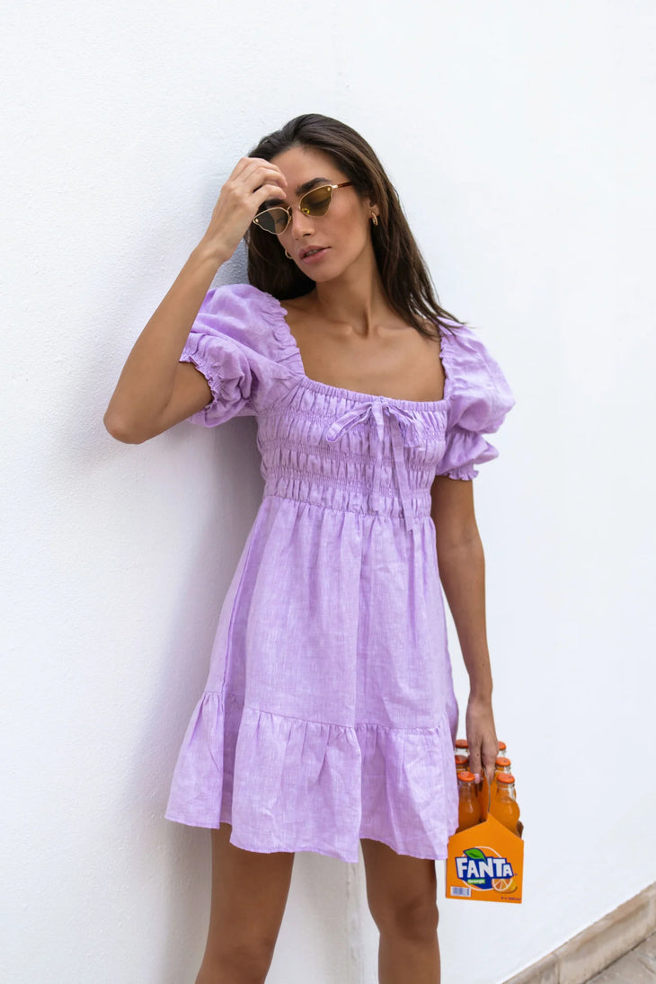 Lilac linen mini dress with puff sleeves and smocked bodice, styled with sunglasses and orange Fanta bottles — Else Adelia | Endless UAE