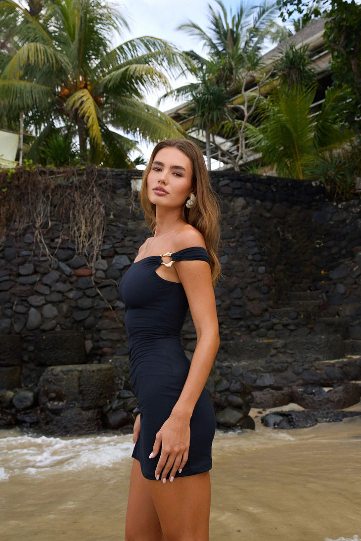Woman wearing black off-shoulder Soléa dress standing in tropical beach setting — Sakuranna | Endless UAE