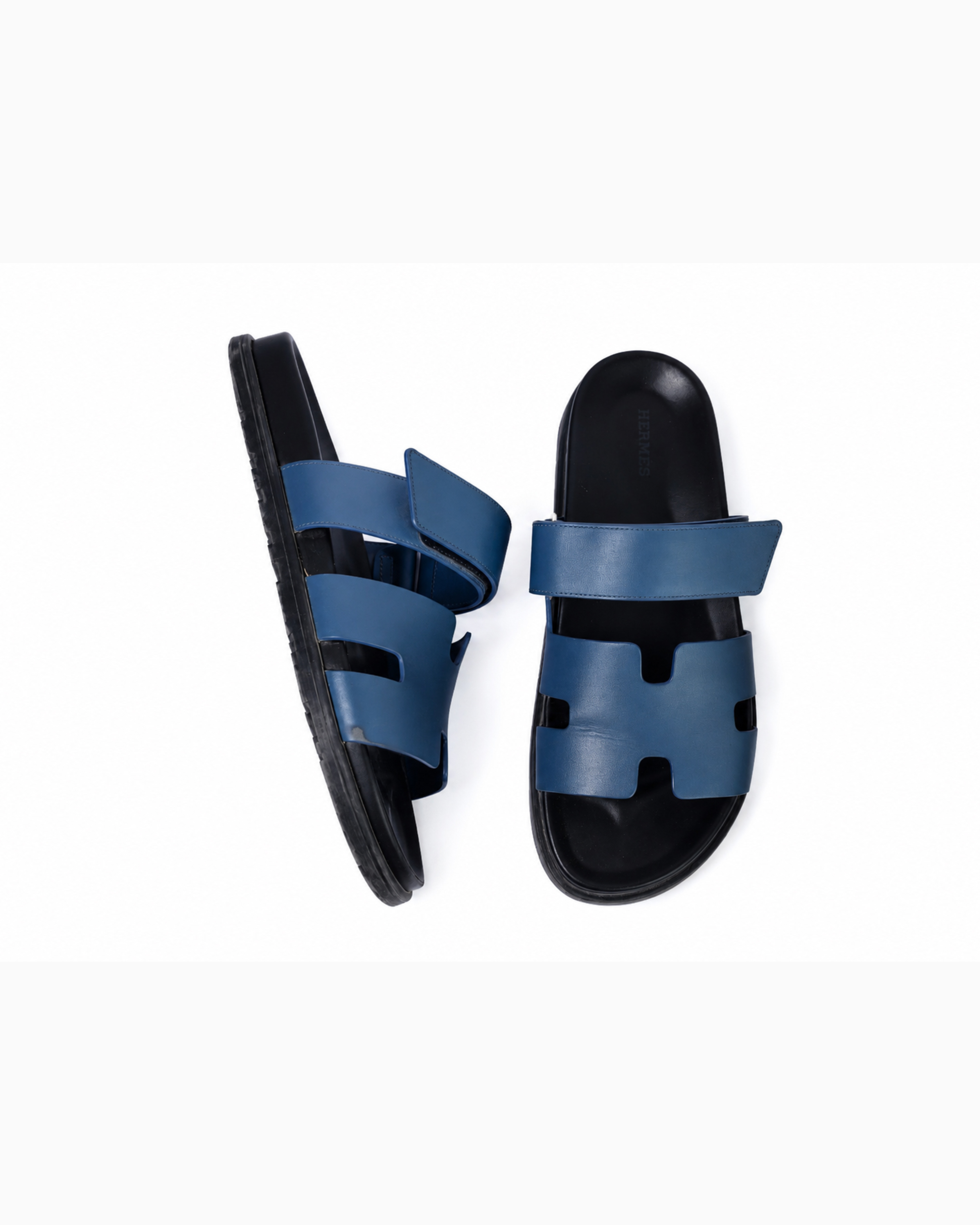 Black leather slide sandals with cutout straps displayed on orange box — Hermès | Endless UAE