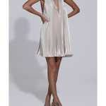 Woman wearing champagne pleated halterneck mini dress with deep V-neckline and metallic heeled sandals — L'IDÉE | Endless UAE