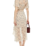 Rear view of woman wearing cream floral-print midi dress with flutter sleeves and shirred waist, holding burgundy handbag — Maje | Endless UAE