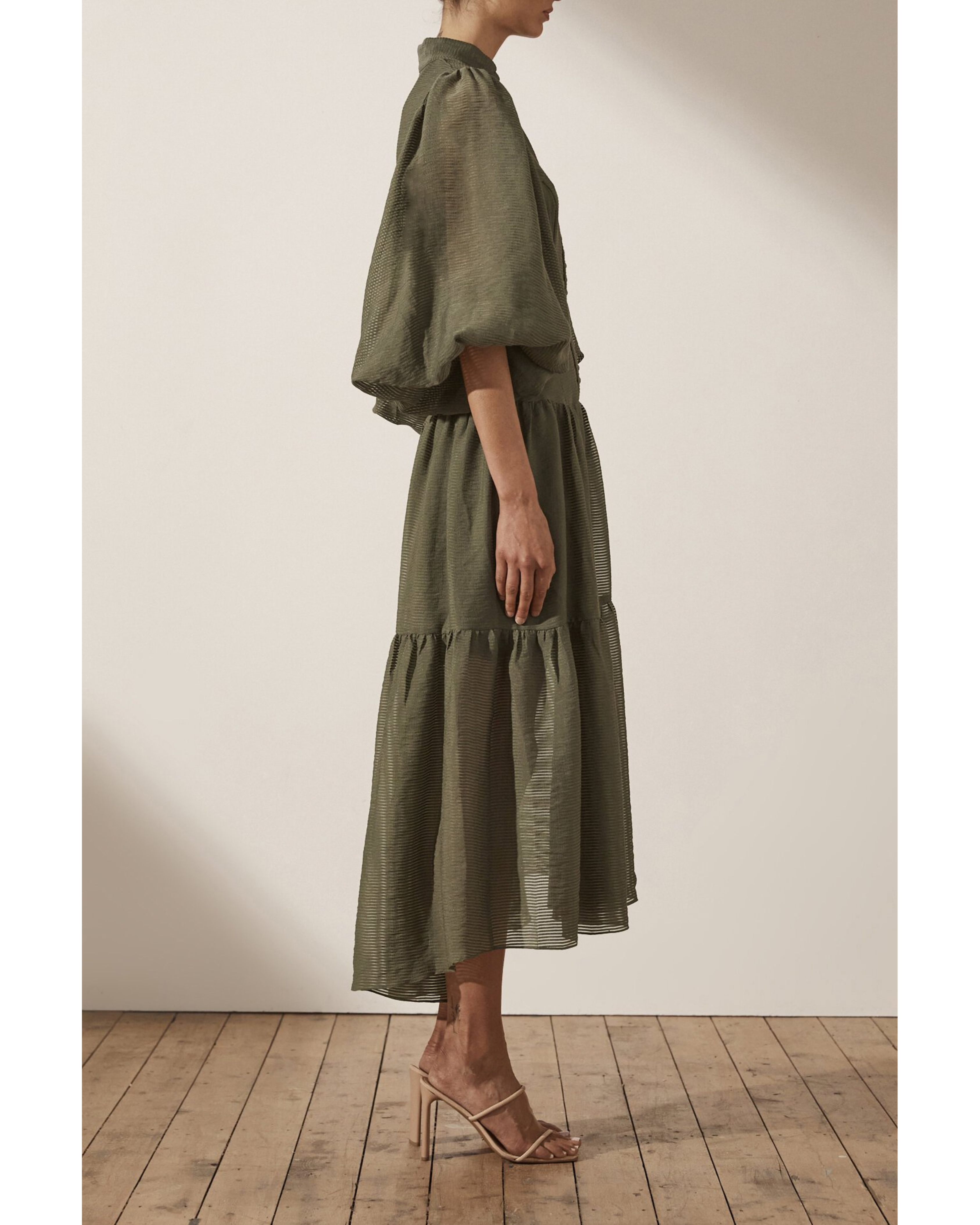 Olive green midi dress with high neck, puffed sleeves, tiered skirt, and textured fabric on model from side view — Shona Joy | Endless UAE