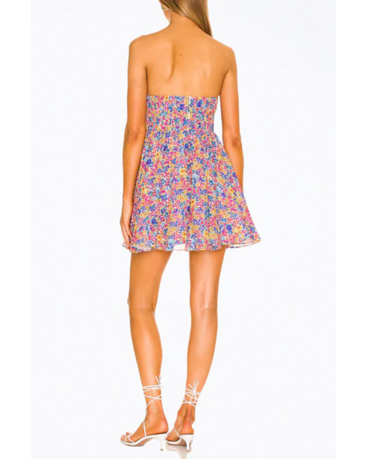 Rear view of woman wearing colorful floral print strapless mini dress with fitted bodice and flared skirt, paired with white heeled sandals — For Love & Lemons | Endless UAE