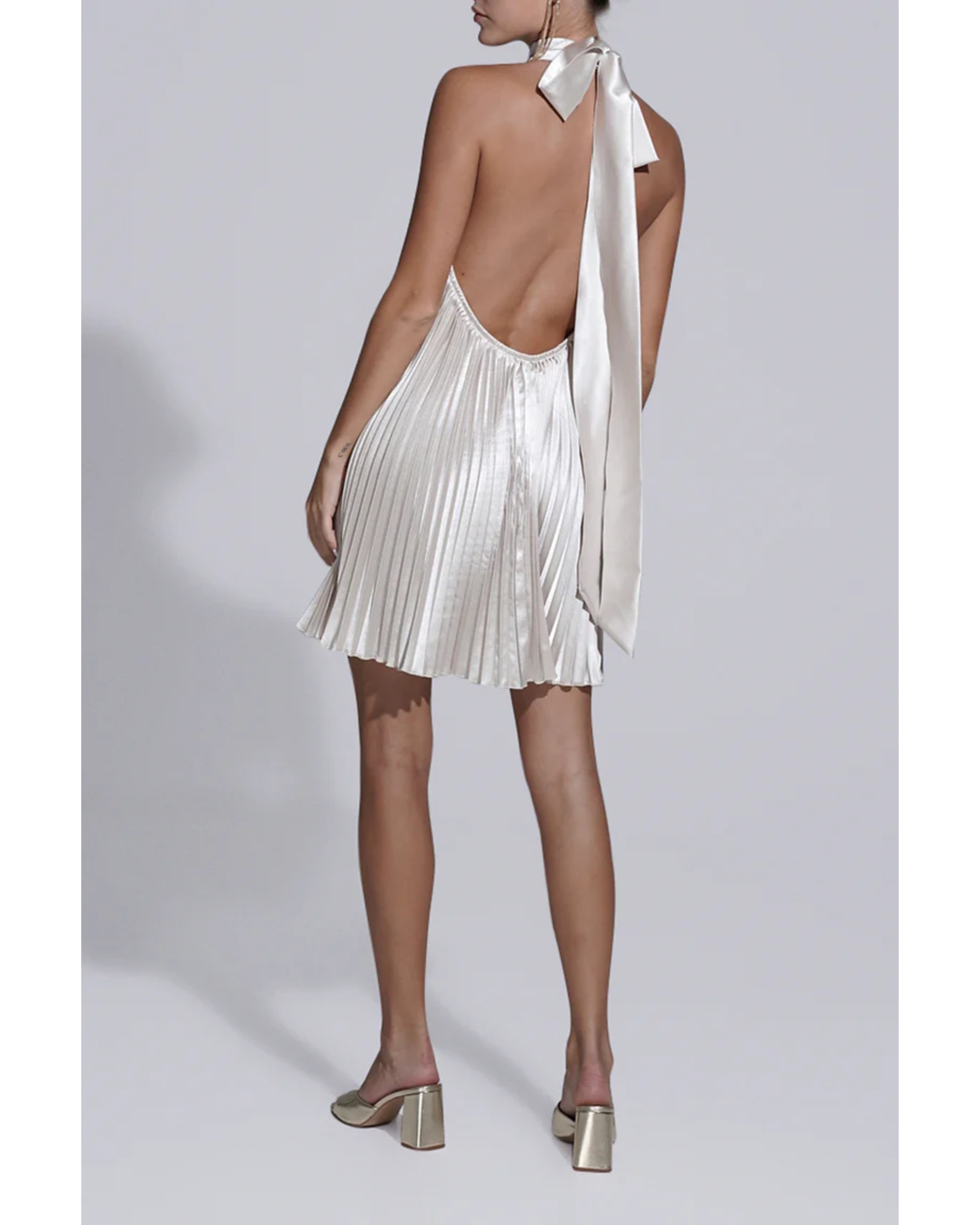 Woman wearing champagne pleated halterneck mini dress with deep V-neckline and metallic heeled sandals — L'IDÉE | Endless UAE