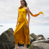 Woman wearing golden yellow silk slip dress standing on rocks by the sea — Vasiliki | Endless UAE