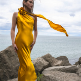 Woman wearing golden yellow silk slip dress standing on rocks by the sea — Vasiliki | Endless UAE