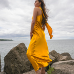 Woman wearing golden yellow silk slip dress standing on rocks by the sea — Vasiliki | Endless UAE
