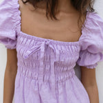Lilac linen mini dress with puff sleeves and smocked bodice, styled with sunglasses and orange Fanta bottles — Else Adelia | Endless UAE