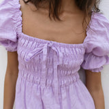 Lilac linen mini dress with puff sleeves and smocked bodice, styled with sunglasses and orange Fanta bottles — Else Adelia | Endless UAE