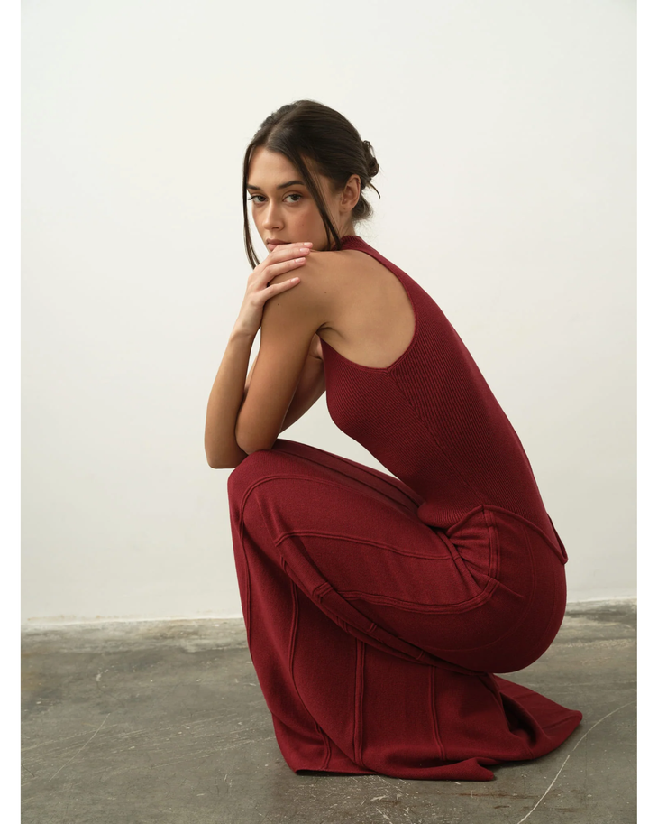 Woman in burgundy ribbed tank maxi dress crouching on concrete floor against white wall — Nora The Label | Endless UAE
