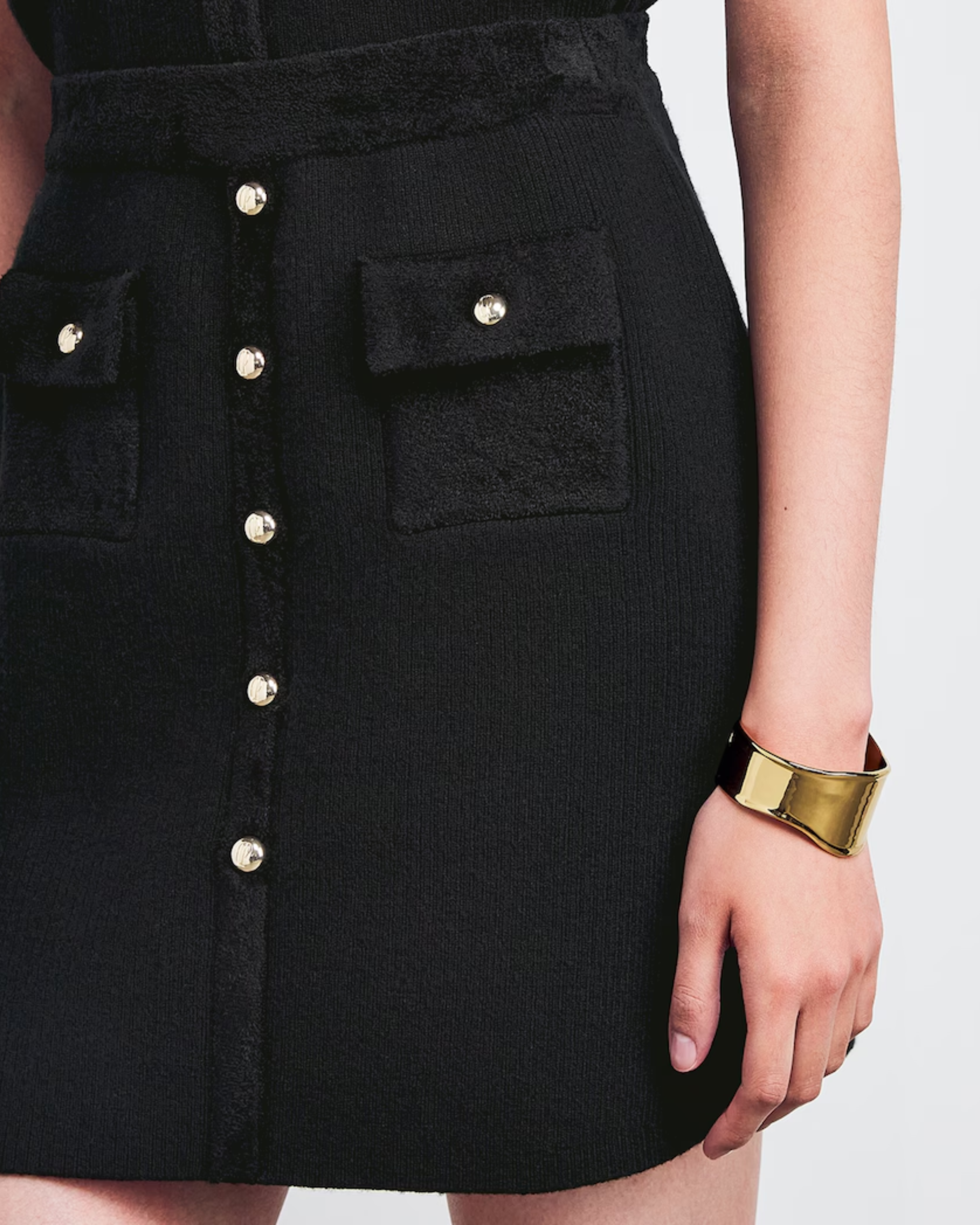 Black knitted mini skirt with silver button front detail and patch pockets, styled with gold cuff bracelet — Claudie Pierlot | Endless UAE