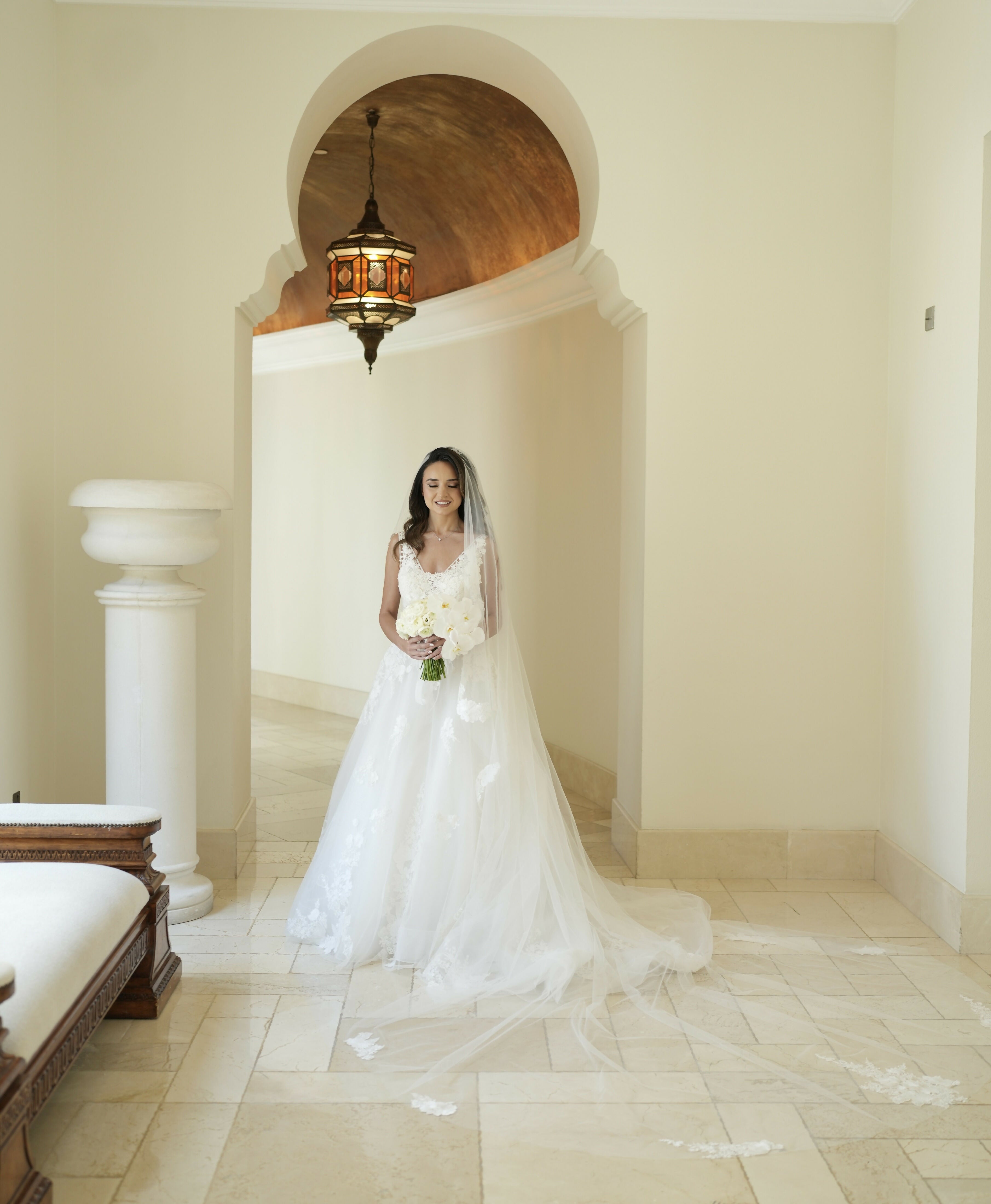 Bride in elegant white lace wedding gown with long veil and bouquet standing in archway — Rosa Clara | Endless UAE