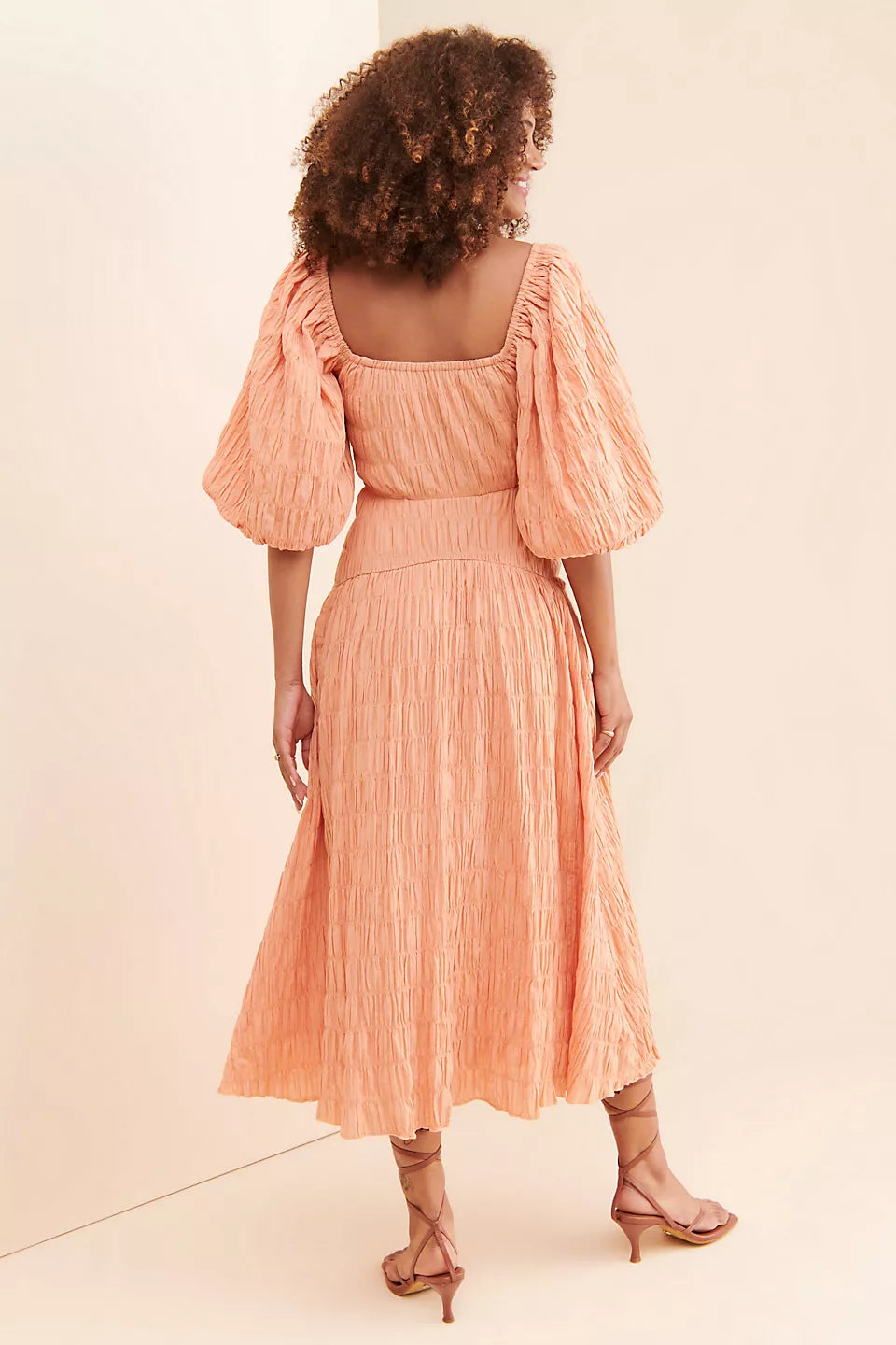 Back view of woman wearing peach textured midi dress with puff sleeves and square neckline — Soverè | Endless UAE