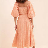 Back view of woman wearing peach textured midi dress with puff sleeves and square neckline — Soverè | Endless UAE