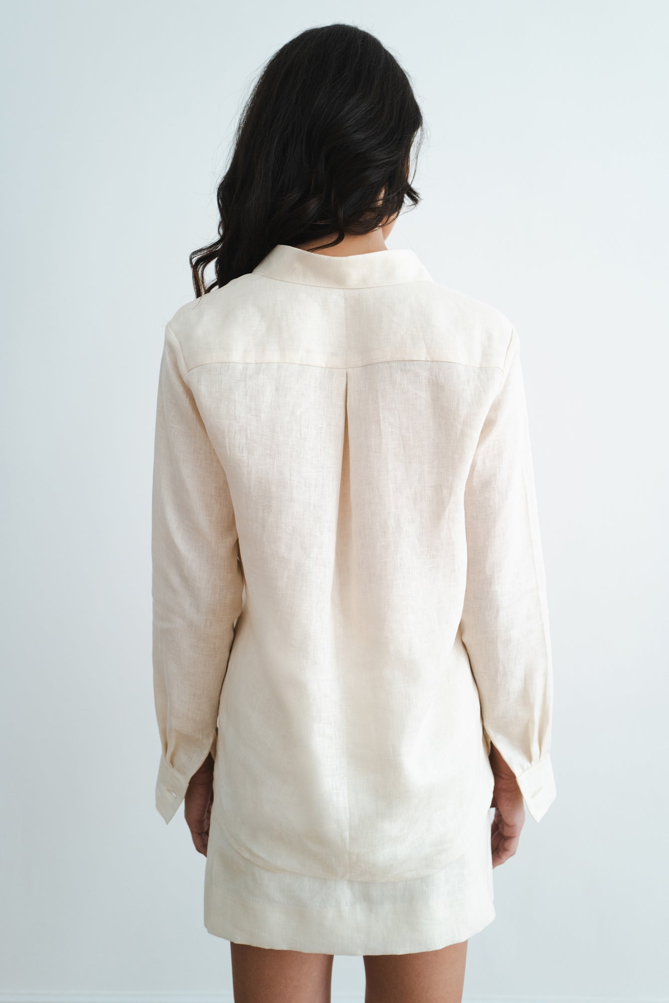 Back view of woman wearing cream linen long-sleeve shirt and shorts set against white background — Amara Grace | Endless UAE