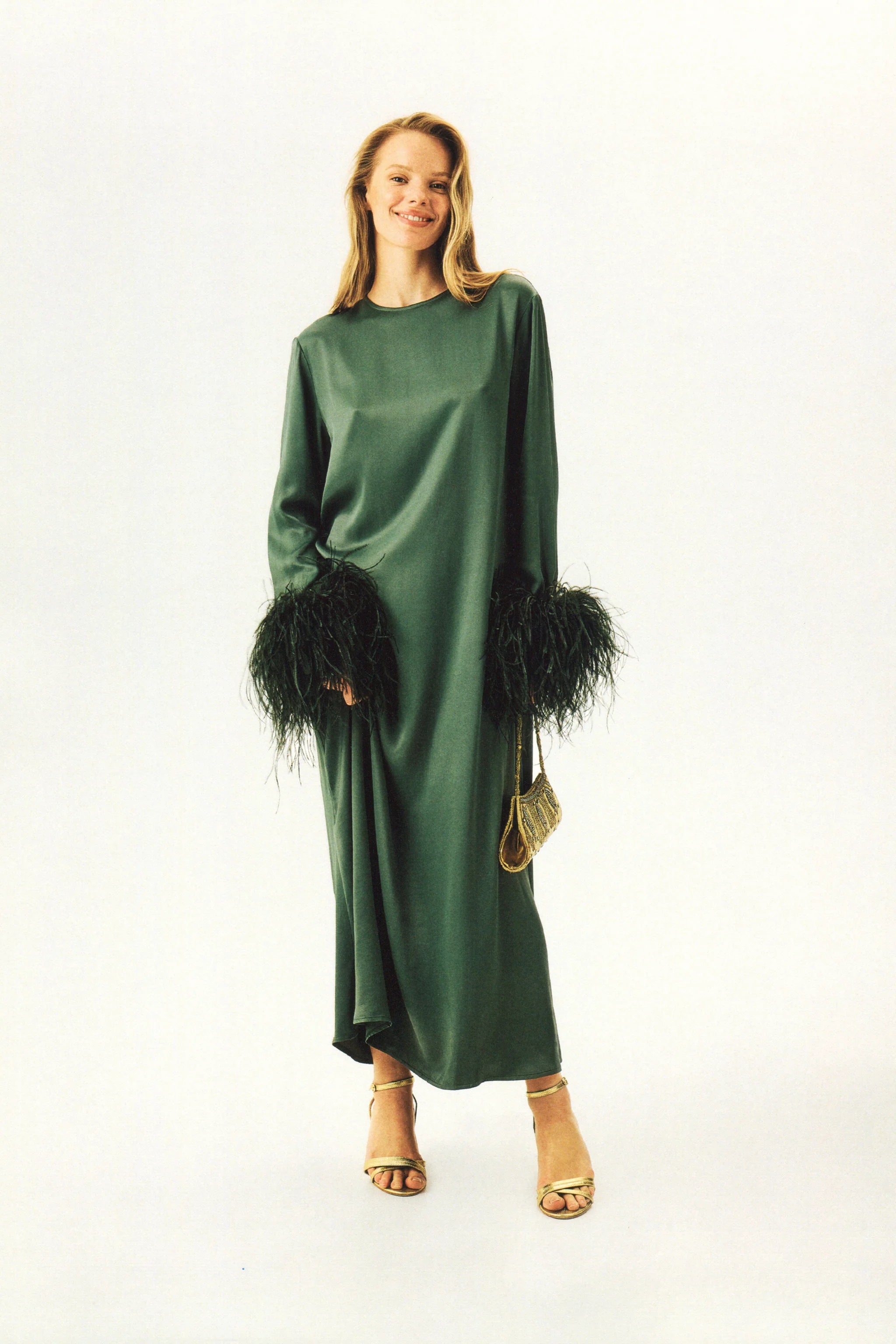 Woman wearing forest green satin midi dress with black feather cuffs and gold sandals — Sleeper | Endless UAE