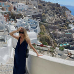 Woman wearing navy sleeveless maxi dress on Santorini terrace overlooking white buildings and sea — AG Studio | Endless UAE