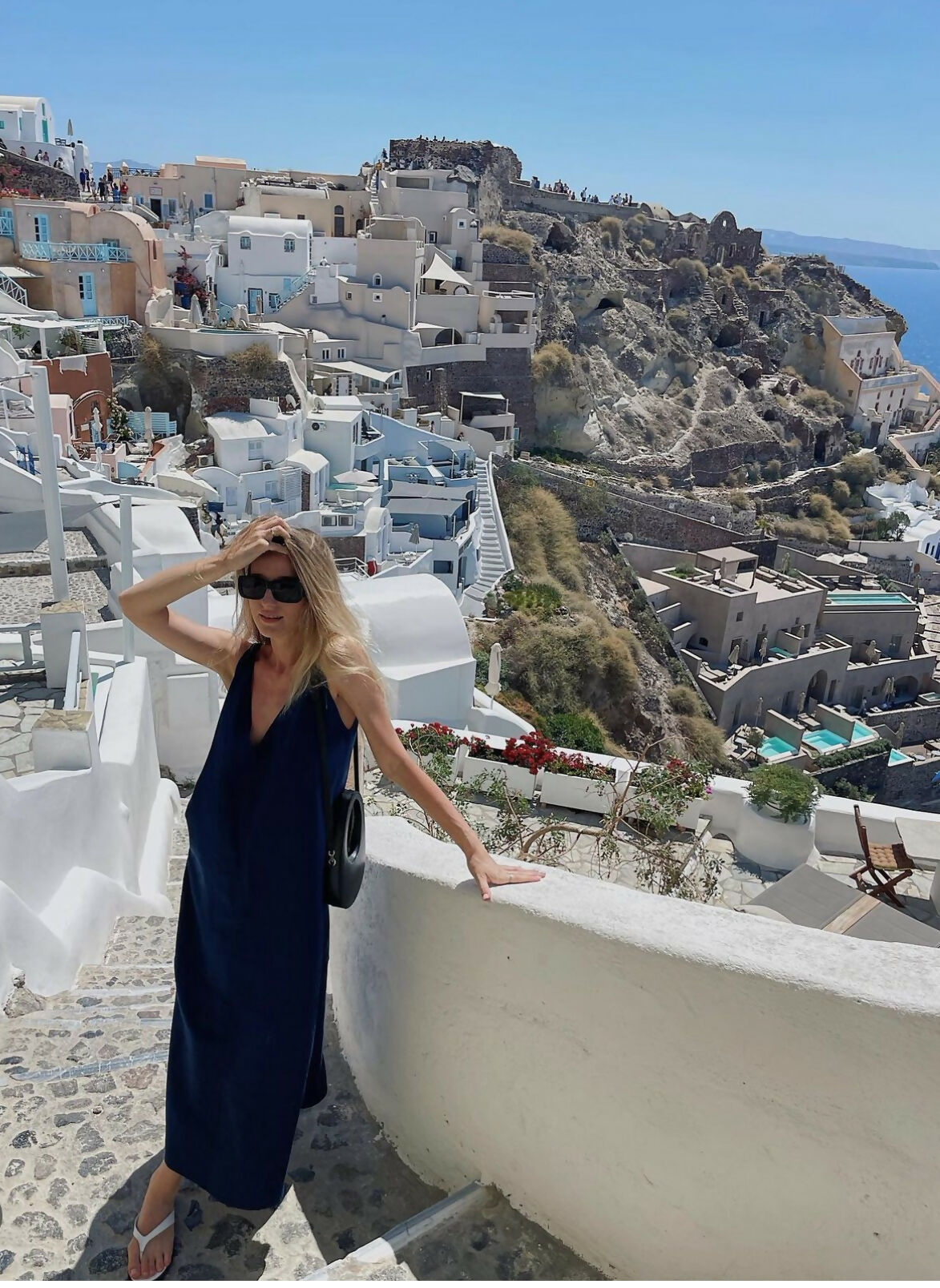 Woman wearing navy sleeveless maxi dress on Santorini terrace overlooking white buildings and sea — AG Studio | Endless UAE