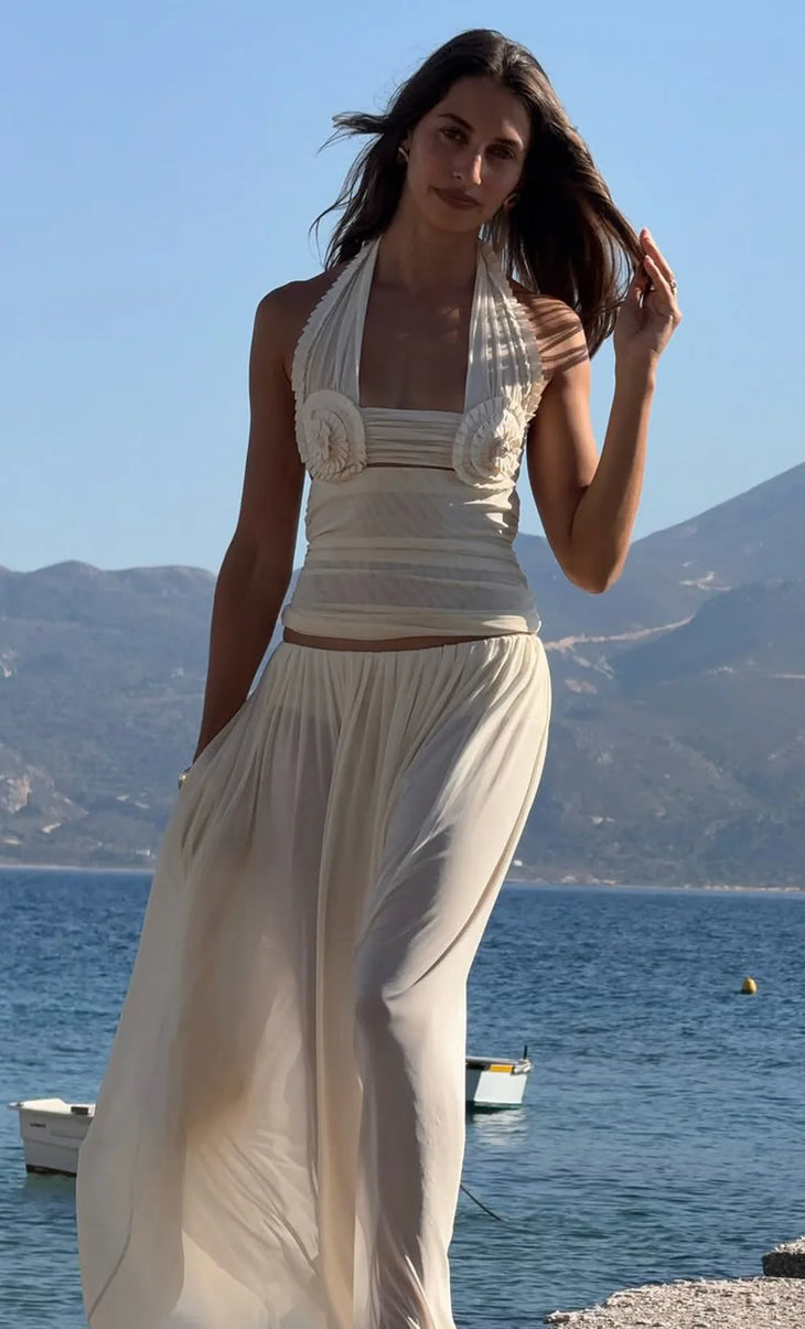 Woman wearing white halter crop top and flowing wide-leg pants by waterside with mountains in background — Bec + Bridge | Endless UAE