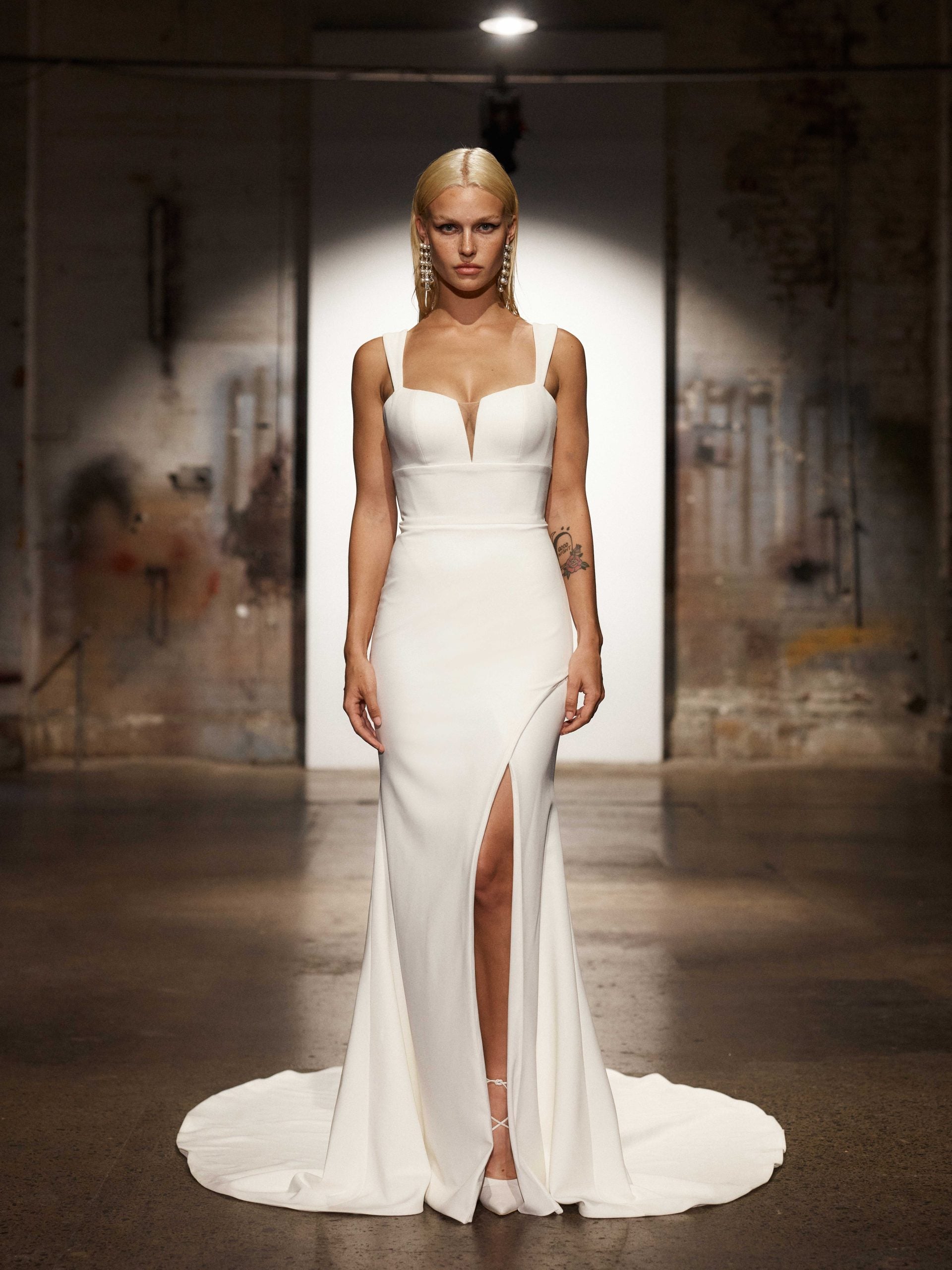 Sleek white wedding gown with plunging neckline, high leg slit, and statement crystal earrings — You&I Bridal | Endless UAE