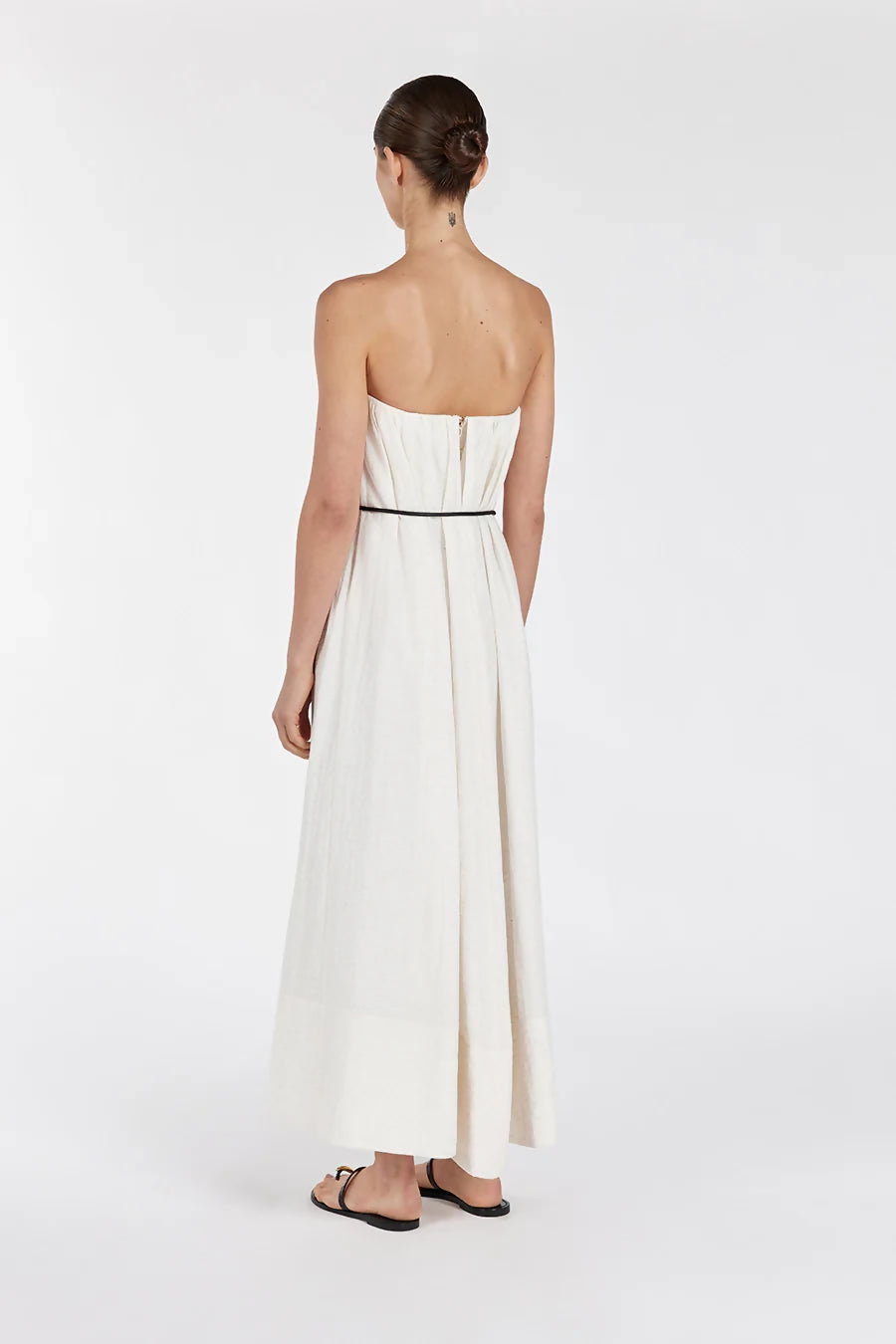 Back view of woman wearing cream strapless midi dress with black waist belt and sandals on white background — Dissh | Endless UAE
