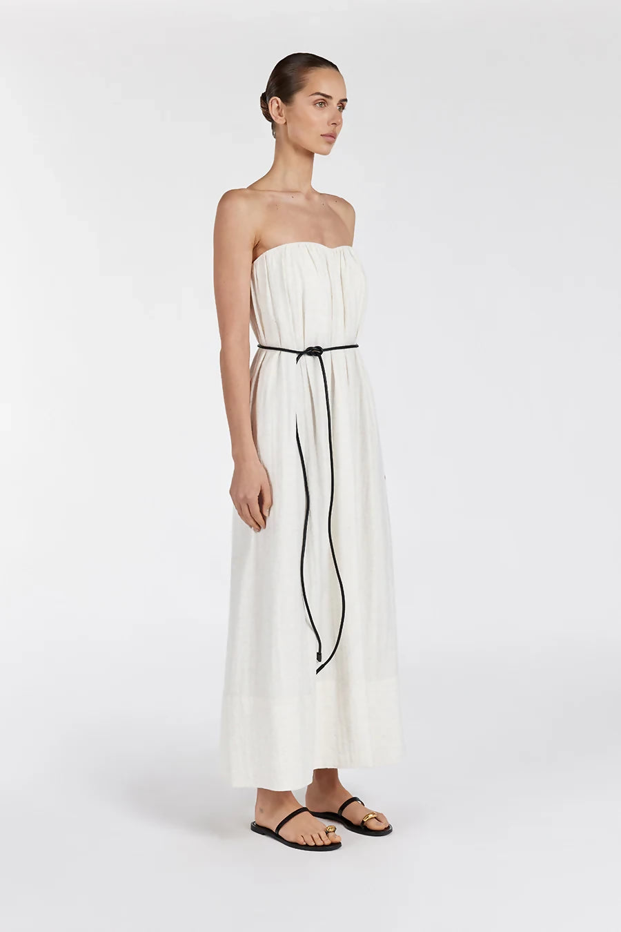 Woman wearing strapless cream marle midi dress with black tie belt and black sandals on white background — Dissh | Endless UAE