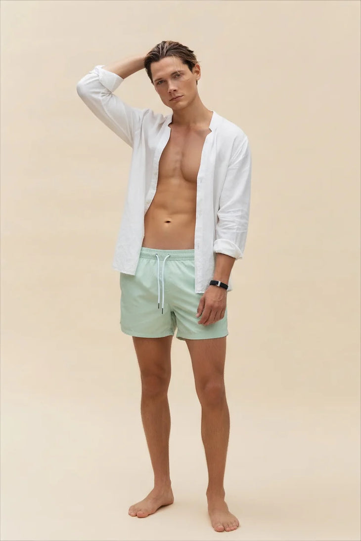 Man wearing unbuttoned off white linen shirt with mint shorts against beige background — Miharo | Endless UAE