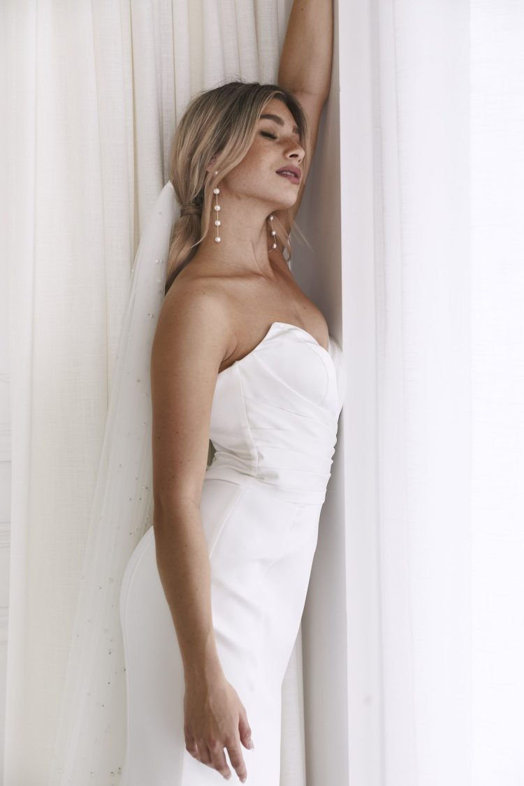 Elegant strapless white bridal gown with draped bodice and pearl drop earrings — You&I Bridal | Endless UAE