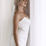 Elegant strapless white bridal gown with draped bodice and pearl drop earrings — You&I Bridal | Endless UAE