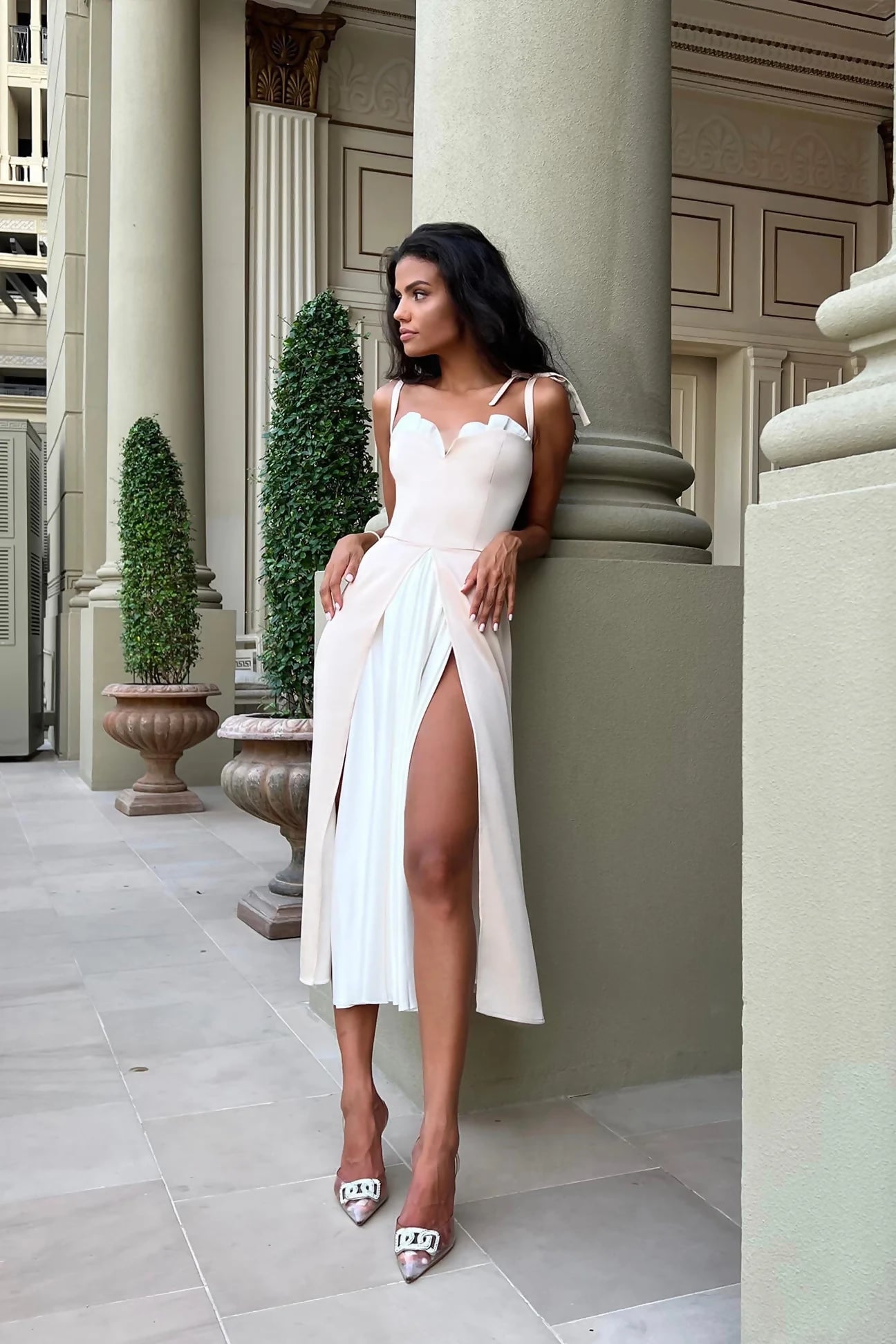 Elegant white midi dress with sweetheart neckline and high slit, modeled in classical architectural setting — Post Meridien | Endless UAE