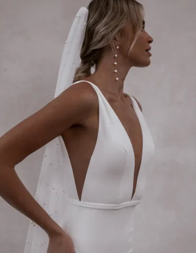 Minimalist white crepe wedding dress with deep V-neckline and pearl-embellished veil — Made with Love | Endless UAE