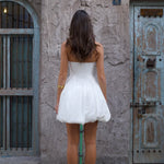 Woman in white strapless midi dress with pleated skirt and white heels against rustic wall — Cleopatress | Endless UAE