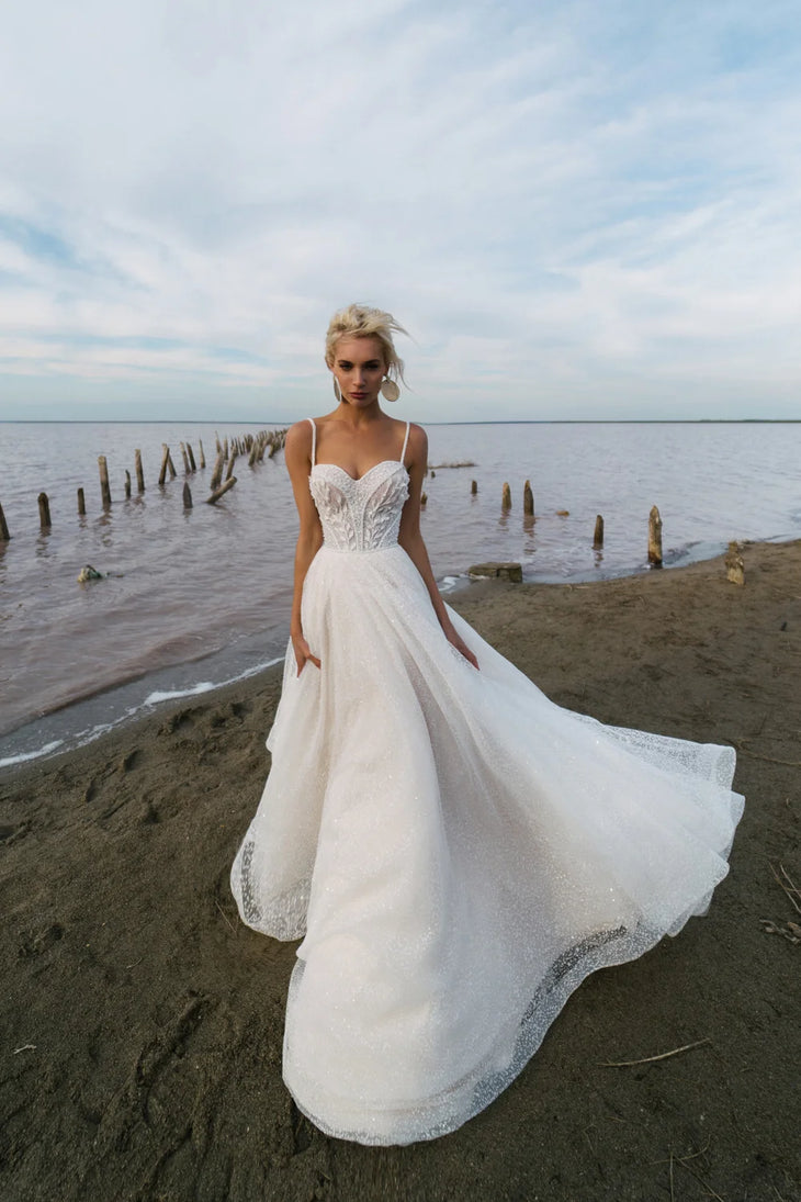 Flowing A-line wedding gown with embellished sweetheart bodice and sparkle tulle skirt by model on beach — Romanova Atelier | Endless UAE