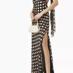 Woman wearing black and cream polka-dot halter maxi dress with side slit and attached scarf, holding white handbag — Alexandra Miro | Endless UAE